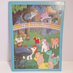May include: A vintage My Little Pony book cover featuring a colorful illustration. The image includes several ponies with various hair colors, a rainbow, and the text "My Little Pony". A whimsical scene with a dwarf is also present.