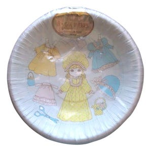 May include: A vintage paper bowl with a light blue background and a design featuring a doll and various dresses. The bowl is 8 6/8 inches in diameter. The doll is wearing a yellow dress and bonnet.