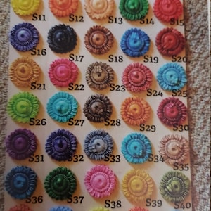May include: A chart of 48 small, round, decorative buttons with a sunflower design. The buttons are arranged in rows and columns and are painted in various colors, including red, blue, green, yellow, orange, and purple.