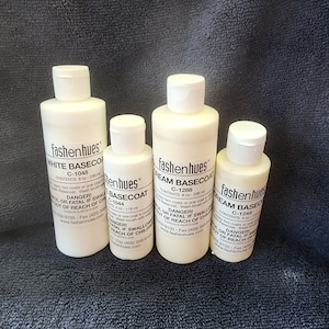 May include: Four bottles of Fashenhues basecoat in varying sizes. The bottles are white with white caps and labels. The labels read "White Basecoat", "Cream Basecoat", and include the size in fluid ounces. The background is a dark blue.