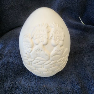 May include: White ceramic egg-shaped ornament with three gnomes sitting on a brick wall. The gnomes have beards and pointy hats.