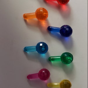 May include: Assortment of colorful, faceted Christmas tree light bulbs. The bulbs are clear, red, orange, blue, teal, green, pink, yellow, and purple.