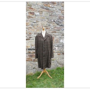 Pode incluir: Um casaco comprido de xadrez marrom e preto com fecho de botão. O casaco está em um manequim de madeira e é exibido contra uma parede de pedra.