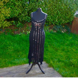 Könnte beinhalten: Ein schwarzes Paillettenkleid mit silbernem und rosafarbenem Design. Das Kleid hat ein figurbetontes Oberteil und einen fließenden Rock.