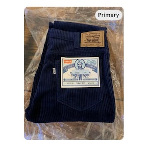 May include: Dark navy corduroy trousers with a tight fit. The trousers have a classic five-pocket design and a Levi Strauss & Co. label on the back pocket. The trousers are folded and displayed on a clear plastic sheet.