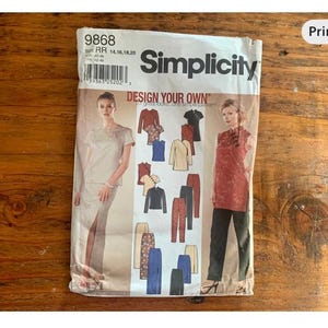 May include: A Simplicity sewing pattern envelope featuring a woman in a skirt suit and a woman in a red top and black pants. The envelope has the text "DESIGN YOUR OWN" and the brand name "Simplicity". The background is a wooden surface.