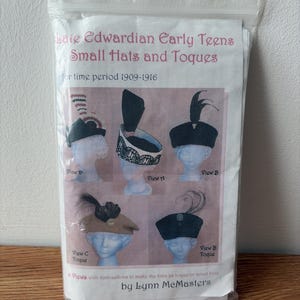 May include: A sewing pattern packet titled Late Edwardian Early Teens Small Hats and Toques for time period 1909-1916 by Lynn McMasters. The front displays five illustrations of various hat styles labelled View D, View A, View B, View C Toque, and View B Toque.