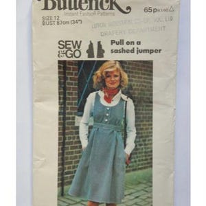 Op de afbeelding: Een vintage naaipatroon voor een getailleerde trui. Het patroon is voor maat 12, borstomvang 87 cm. Het patroon is van Butterick en heeft nummer 4602. Het patroon toont een vrouw die een blauw-wit gestreepte trui draagt met een wit blouse en een rode sjaal.