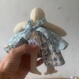 Pu&ograve; includere: Bambola fatta a mano con testa e arti color crema, indossa un vestito a fantasia floreale blu e bianco. L'abito ha un mantello a pois azzurri e un fiocco al collo. La bambola &egrave; in tessuto morbido.