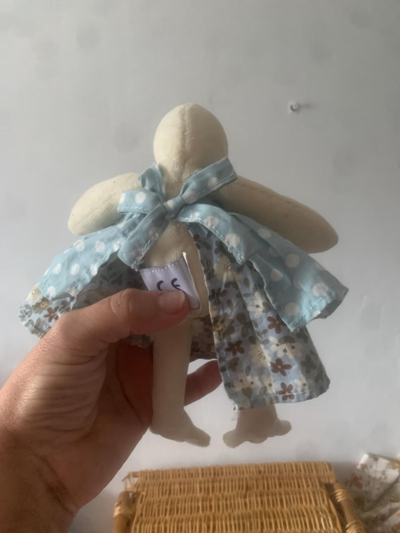 Pu&ograve; includere: Bambola fatta a mano con testa e arti color crema, indossa un vestito a fantasia floreale blu e bianco. L'abito ha un mantello a pois azzurri e un fiocco al collo. La bambola &egrave; in tessuto morbido.