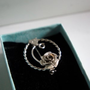May include: A silver brooch in the shape of a rose with a twisted wire design. The brooch is in a blue velvet box.