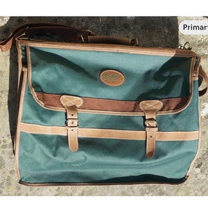 May include: A green canvas travel bag with brown leather accents and buckles. The bag has a brown leather strap and a logo that says "Cotswold" in green lettering.