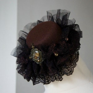 Brown Mini Hat With Dark Brown Net And Lace And Decorated With Brass Coloured Pendant With Watch Cog Detail And Brass And Gold Colour Beads