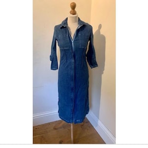 May include: A long-sleeved denim dress with a collared neckline and a zipper closure. The dress is a dark blue color and has a fitted silhouette.