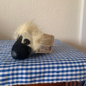 May include: A small, black and white plush toy dog with a brown nose and large black eyes. The dog is sitting on a blue and white checkered fabric.