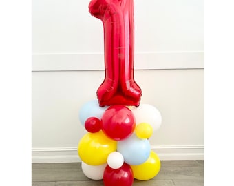 May include: A red number one foil balloon atop a cluster of colorful balloons. The balloons are red, yellow, white, and light blue. This festive arrangement is suitable for a first birthday celebration or other milestone event.