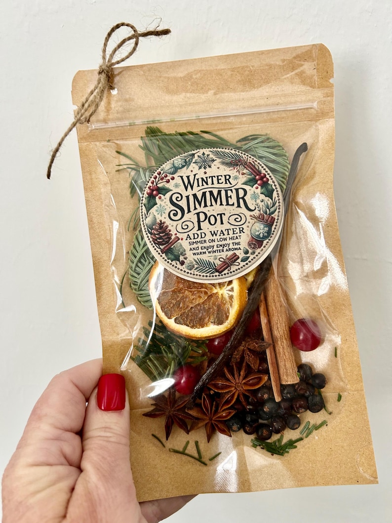 Pu&ograve; includere: Un sacchetto di plastica trasparente pieno di ingredienti per un simmer pot invernale. Il sacchetto ha un esterno di carta marrone con un'etichetta che recita "Winter Simmer Pot" e istruzioni per aggiungere acqua e far sobbollire a fuoco lento. Gli ingredienti includono fette d'arancia, bastoncini di cannella, anice stellato, bacche di ginepro e rametti di sempreverdi.