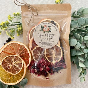 Pu&ograve; includere: Un sacchetto di plastica trasparente pieno di frutta di agrumi secca, petali di rosa e bacche di ginepro. Il sacchetto &egrave; legato con uno spago e ha un'etichetta che recita "Citrus & Blooms Simmer Pot". L'etichetta include anche le istruzioni per l'utilizzo degli ingredienti per preparare un simmer pot.