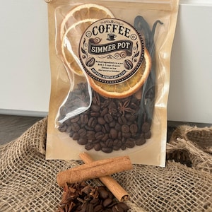May include: A clear plastic bag filled with coffee beans, cinnamon sticks, star anise, dried orange slices, and vanilla beans. The bag has a label that reads "Coffee Simmer Pot" and includes instructions for making a coffee simmer pot.