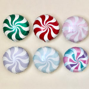 May include: Six round foil balloons shaped like peppermint candies. The balloons are in various colors, including green, red, pink, purple, blue, and white.