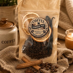 May include: A clear plastic pouch with a kraft paper top containing a coffee simmer pot blend. The label reads COFFEE SIMMER POT with instructions. Inside are whole coffee beans, dried orange slices, and vanilla beans. Two cinnamon sticks and star anise sit in front.