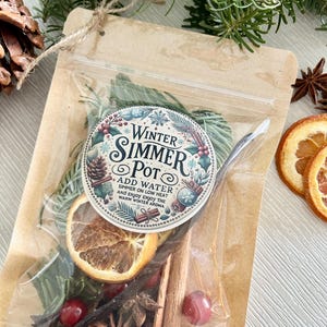 Pu&ograve; includere: Un sacchetto di carta marrone con una finestra di plastica trasparente che contiene un mix di frutta secca, spezie ed erbe. Il sacchetto ha un'etichetta che recita "Winter Simmer Pot" con istruzioni per aggiungere acqua e far sobbollire a fuoco lento.