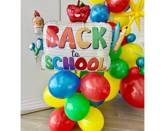 May include: A balloon arch featuring a large "Back to School" balloon in the centre. The arch is made up of red, yellow, blue and green balloons. There are also smaller balloons with school-themed designs, such as an apple, a pencil and a ruler.