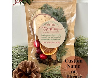 May include: A clear plastic bag filled with dried fruit, spices, and evergreen sprigs. A round label with the text "Merry Christmas and Happy New Year" is attached to the bag. The label also includes the text "May this simmering pot bring warmth, joy, and a touch of holiday spirit to your home! The Smith Family". A second round label is visible with the text "Custom Name or Phrase".