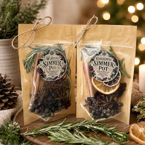 May include: Two brown paper pouches with clear windows containing dried ingredients for a simmer pot. Each pouch is tied with twine and features a circular label reading Winter Simmer Pot or Christmas Simmer Pot with cinnamon, rosemary, and fruit.