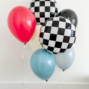 May include: A group of balloons in various colors and patterns, including red, blue, white, and black and white checkered. The balloons are tied together with white curling ribbon.