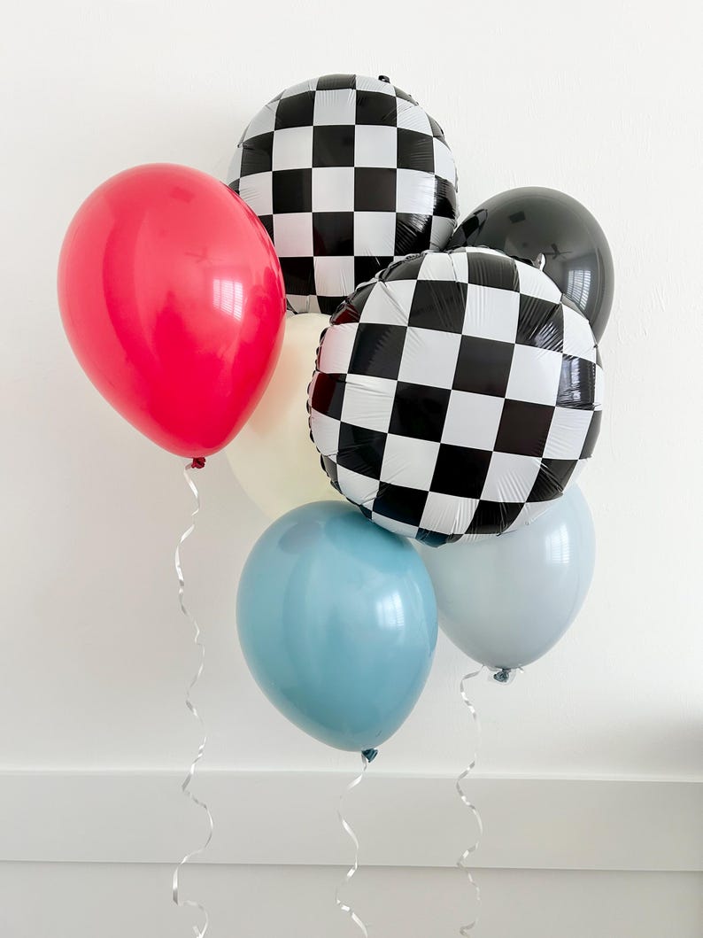 May include: A group of balloons in various colors and patterns, including red, blue, white, and black and white checkered. The balloons are tied together with white curling ribbon.