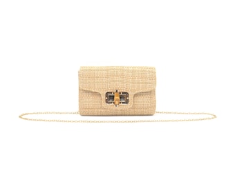 May include: A small, rectangular beige handbag with a woven texture. The bag features a gold-colored chain strap and a rectangular clasp with a gold-colored frame. The bag is set against a white background.