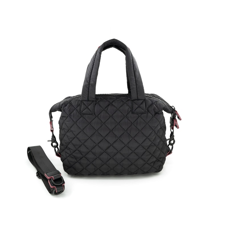 K&ouml;nnte beinhalten: Schwarze, gesteppte Nylon-Tragetasche mit Rei&szlig;verschluss oben, zwei Tragegriffen und einem abnehmbaren Schultergurt. Die Tasche hat ein Rautenmuster und rosa Akzente.