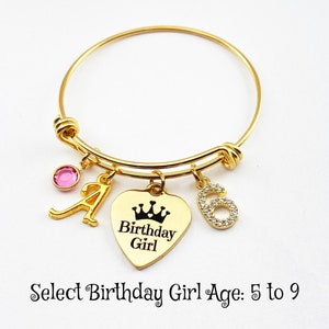 May include: Gold bangle bracelet with a heart charm that says "Birthday Girl" with a crown above the text. The bracelet also has a pink crystal charm and a charm with the number 6 with rhinestones.