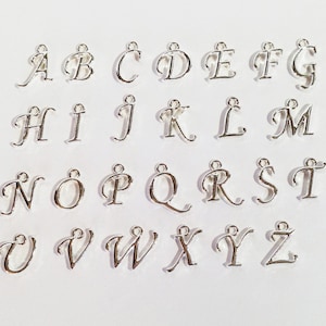 May include: A set of 26 silver-colored metal alphabet letter charms. Each letter is in a cursive font style.