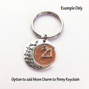 May include: A silver-colored keychain with a penny featuring the number 21. The penny is set in a crescent moon charm with the words "I love you to the moon and back." The keychain is a personalized gift.