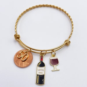 May include: Gold bangle bracelet with a penny charm with the number 30 on it, a wine bottle charm, and a wine glass charm.  Option to Add Wine Bottle & Wine Glass Charm. Example of Bracelet with Added Charms.