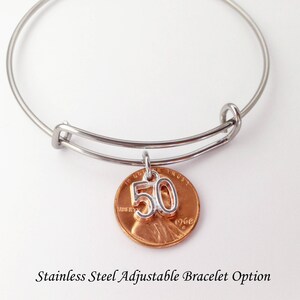 May include: A stainless steel adjustable bangle bracelet with a copper penny charm. The penny has a silver number "50" charm attached. The text "1968" is visible on the penny. The bracelet is a gift for a 50th birthday.