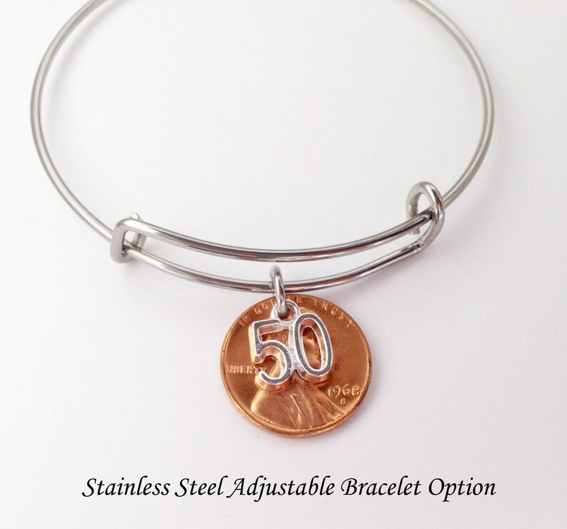 May include: A stainless steel adjustable bangle bracelet with a copper penny charm. The penny has a silver number "50" charm attached. The text "1968" is visible on the penny. The bracelet is a gift for a 50th birthday.