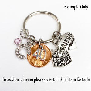 May include: A silver keychain with multiple charms. Charms include a penny with the number 40, a horseshoe with rhinestones, a heart with the word "FRIEND", and a birthday cake. The text "HAPPY BIRTHDAY" is on the cake charm.