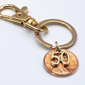 May include: Gold key chain with a copper penny charm featuring the number 50. The penny is dated 1974.