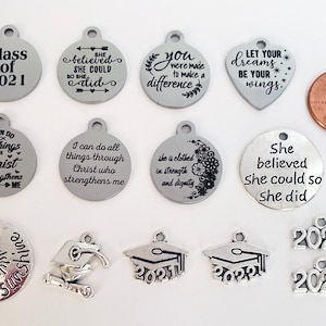 May include: Assortment of silver charm pendants with inspirational and graduation themed messages.  The charms include phrases like "She believed she could so she did", "You were made to make a difference", and "Let your dreams be your wings".  There are also graduation caps with the years 2021 and 2022.