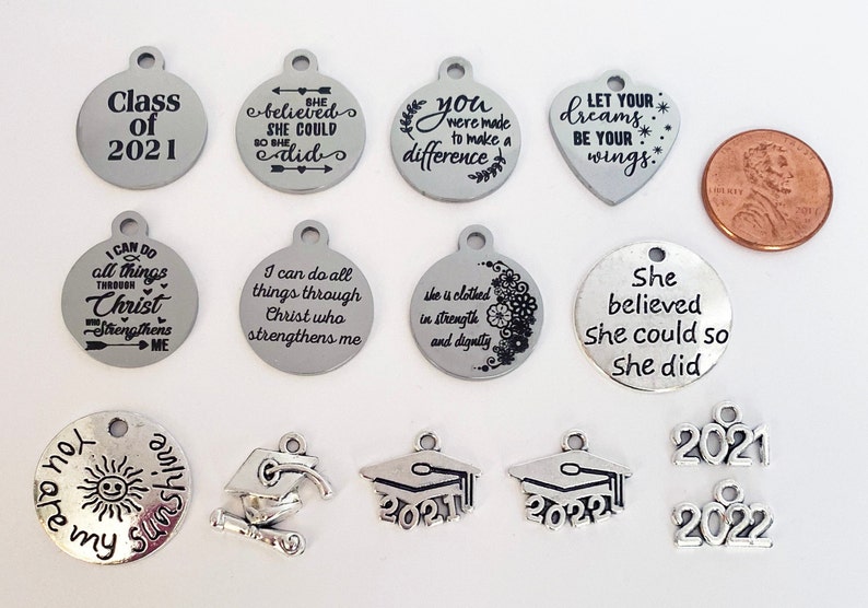 May include: Assortment of silver charm pendants with inspirational and graduation themed messages.  The charms include phrases like "She believed she could so she did", "You were made to make a difference", and "Let your dreams be your wings".  There are also graduation caps with the years 2021 and 2022.