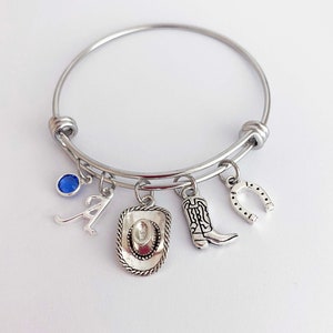 May include: A silver charm bracelet with a blue gemstone, a letter A charm, a cowboy hat charm, a cowboy boot charm, and a horseshoe charm.