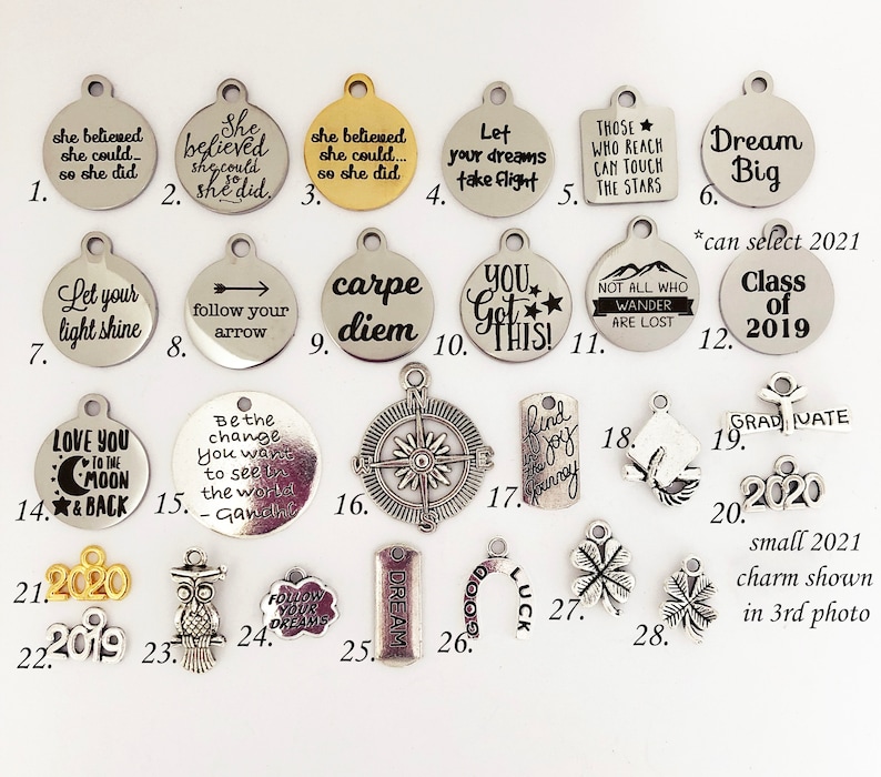 May include: A collection of 28 silver and gold charm pendants with various inspirational quotes and designs. The charms include phrases like "Let your light shine", "Dream Big", "Carpe Diem", "You Got This", and "Follow Your Dreams".