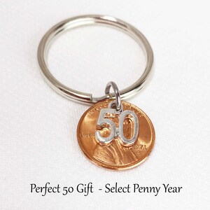 May include: A silver key ring with a copper penny pendant. The penny has a silver '50' charm attached. The text on the penny reads '1971'. The key ring is a perfect gift for a 50th birthday.