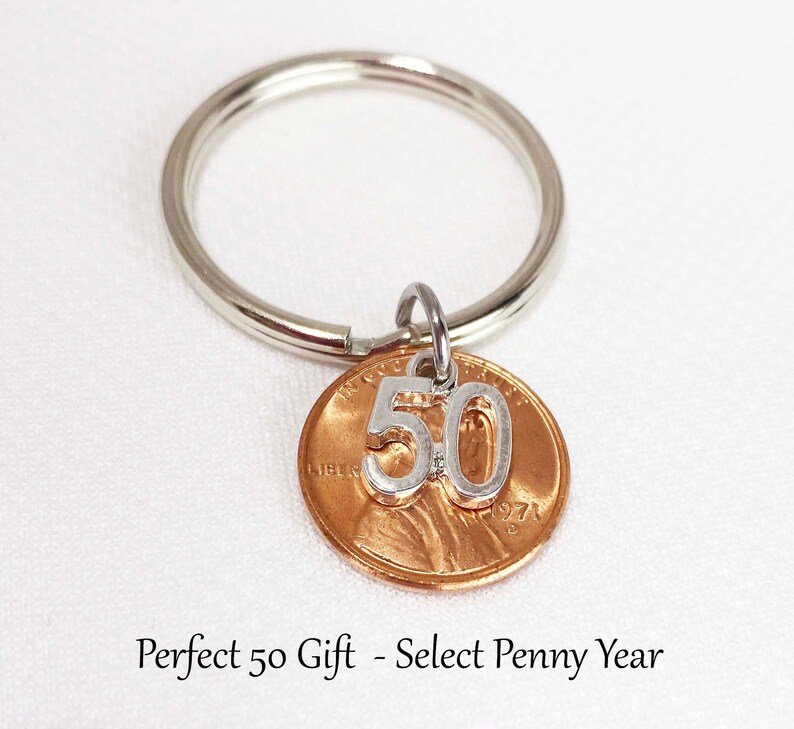 May include: A silver key ring with a copper penny pendant. The penny has a silver '50' charm attached. The text on the penny reads '1971'. The key ring is a perfect gift for a 50th birthday.