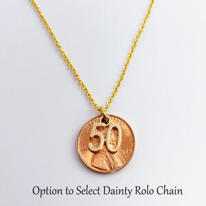 May include: Gold necklace with a copper penny pendant featuring the number 50. The penny is dated 1974. Option to select dainty rolo chain.