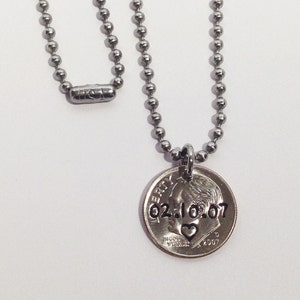 May include: A silver-colored necklace with a ball chain and a coin pendant. The coin is engraved with the date 02.10.07 and a heart symbol. The necklace is displayed against a white background.