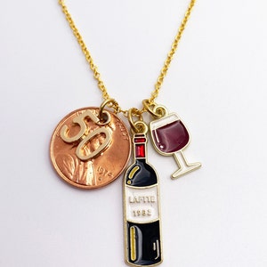 May include: Gold necklace with a 1982 penny charm with the number 50 on it, a wine bottle charm with the text "LAFFITE 1982" and a wine glass charm.